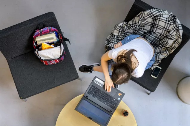 Foto ovanifrån på en student som sitter med sin latop vid en litet kafebord.